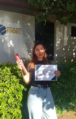 Aluna da FADEC ao ar livre com seu cartão de conclusão